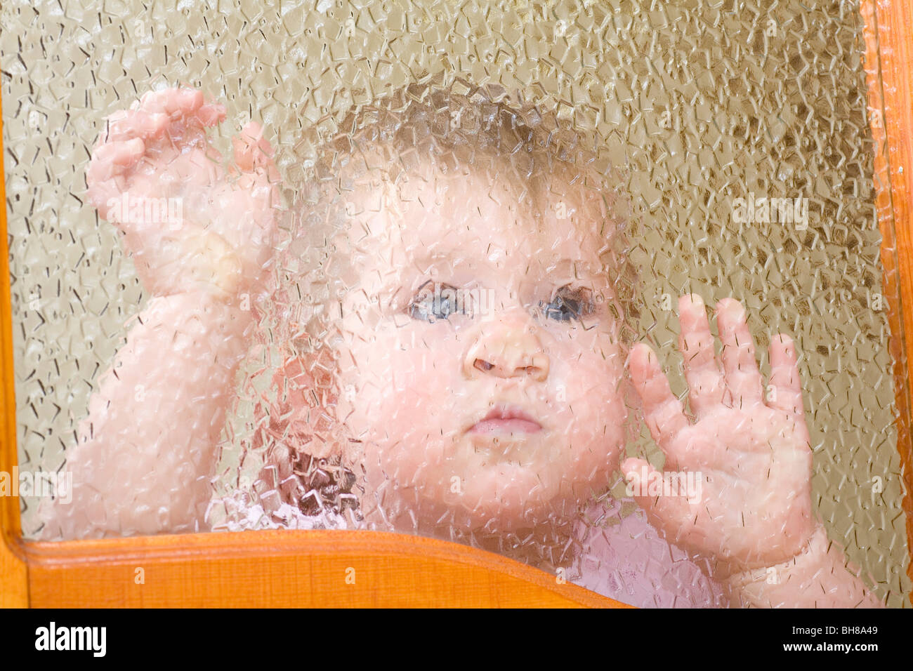 Un bambino premuta contro una parte smussata finestra in vetro Foto Stock