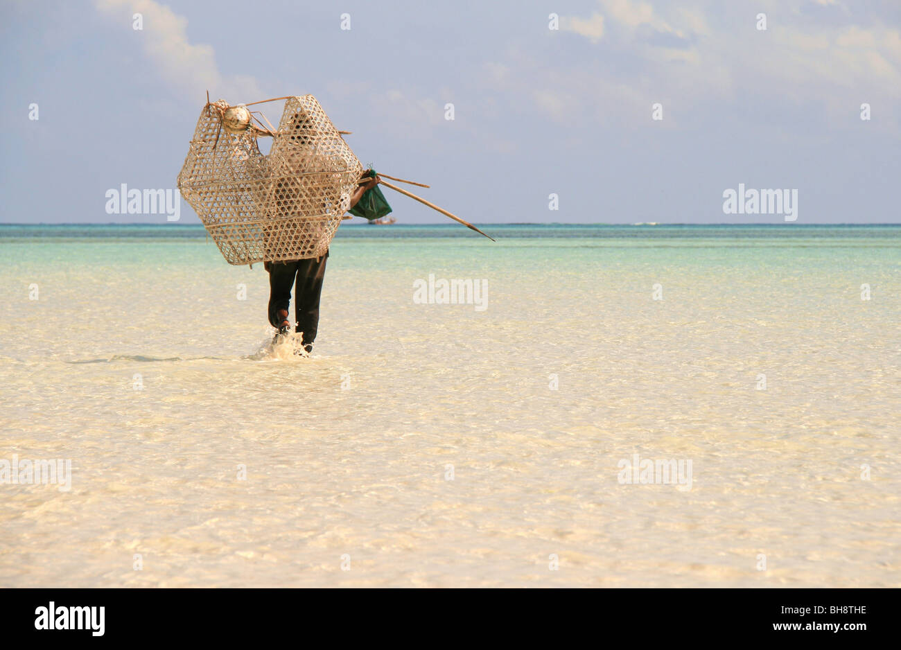 Un pescatore di gamberi con pot wades attraverso turquise acqua di mare a bassa marea off nungwi Beach, il paradiso tropicale a Zanzibar Foto Stock