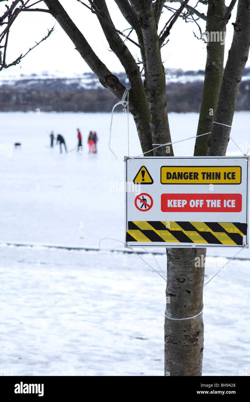 Il cartello di avvertimento di ghiaccio sottile accanto ad un Loch di Sapple del Castello congelato con la gente in inverno, il Parco Regionale di Clyde Muirshiel, Lochwinnoch, Renfrewshire, Scozia, Regno Unito Foto Stock