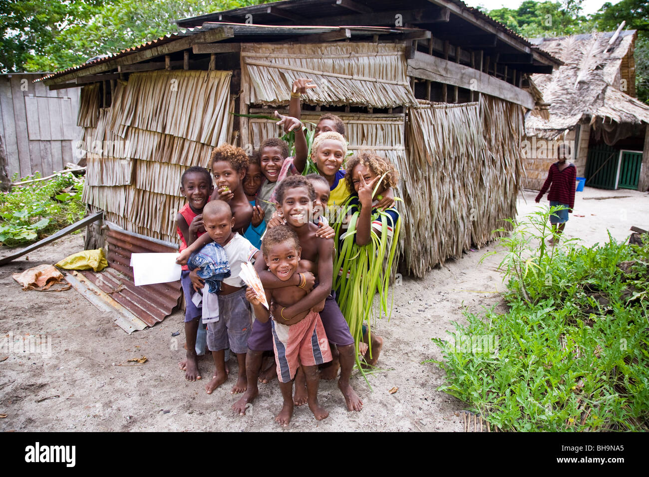 Bambini melanesiano pongono per la fotocamera nella parte anteriore di una capanna con tetto di paglia di Melanesia Foto Stock