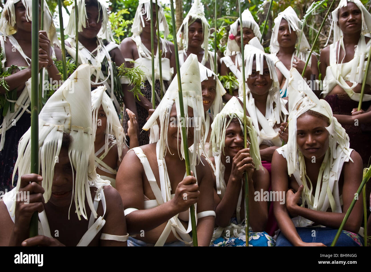 Un gruppo di giovani Melanesian uomini e donne che indossano tradizionali bianche orlate abiti di testa pongono sorridente nella fotocamera Foto Stock
