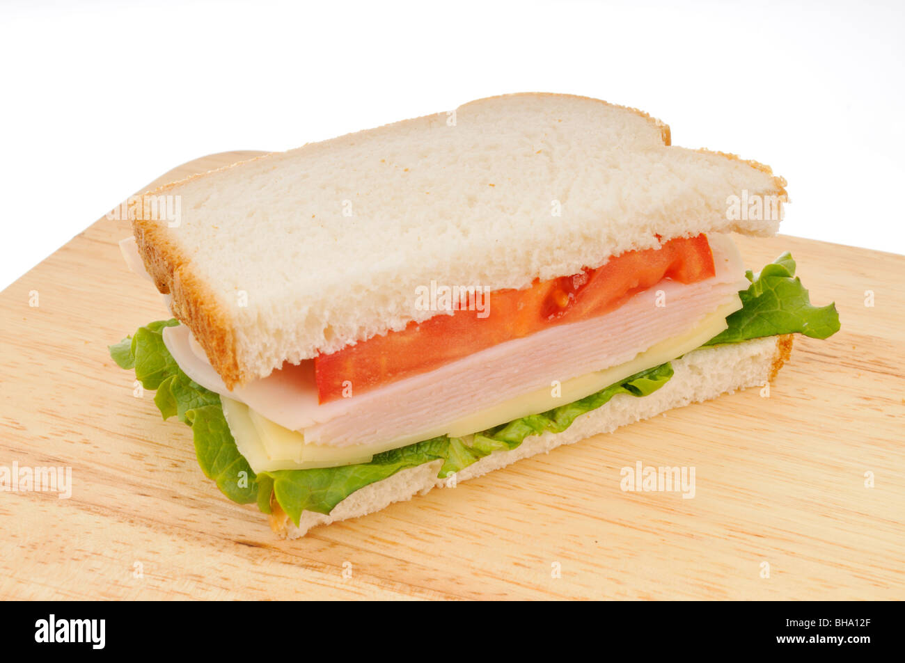 La metà di una Turchia e formaggio in sandwich di pane bianco con lattuga e pomodoro su un tagliere su sfondo bianco. Foto Stock
