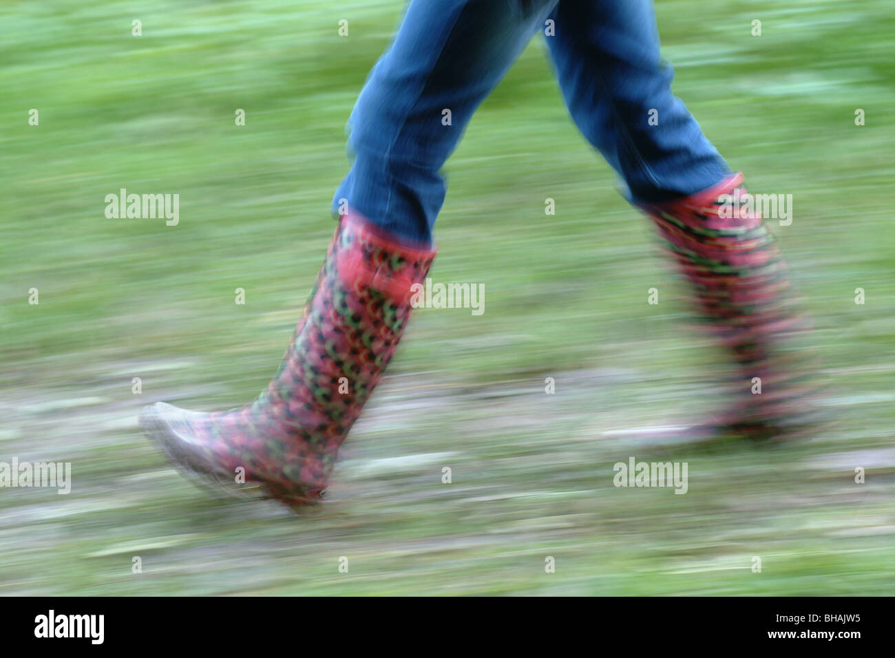 Giovane ragazza in jeans e rosso passeggiate wellingtons rapidamente causando la sfocatura in movimento. Regno Unito Foto Stock