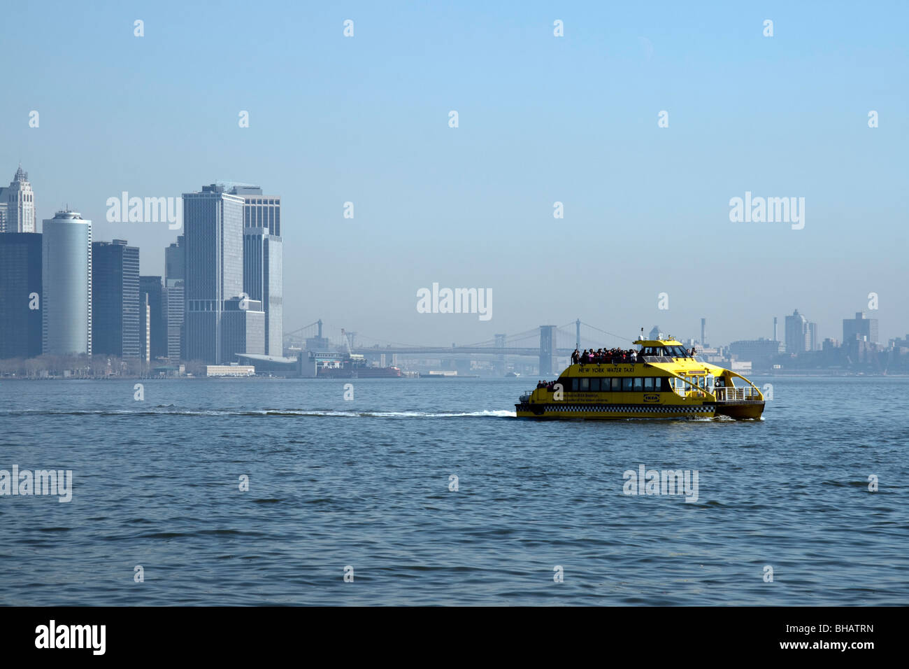 Con un taxi acqueo velocità attraverso l'acqua con la parte inferiore della skyline di Manhattan e ponti visibili in background Foto Stock