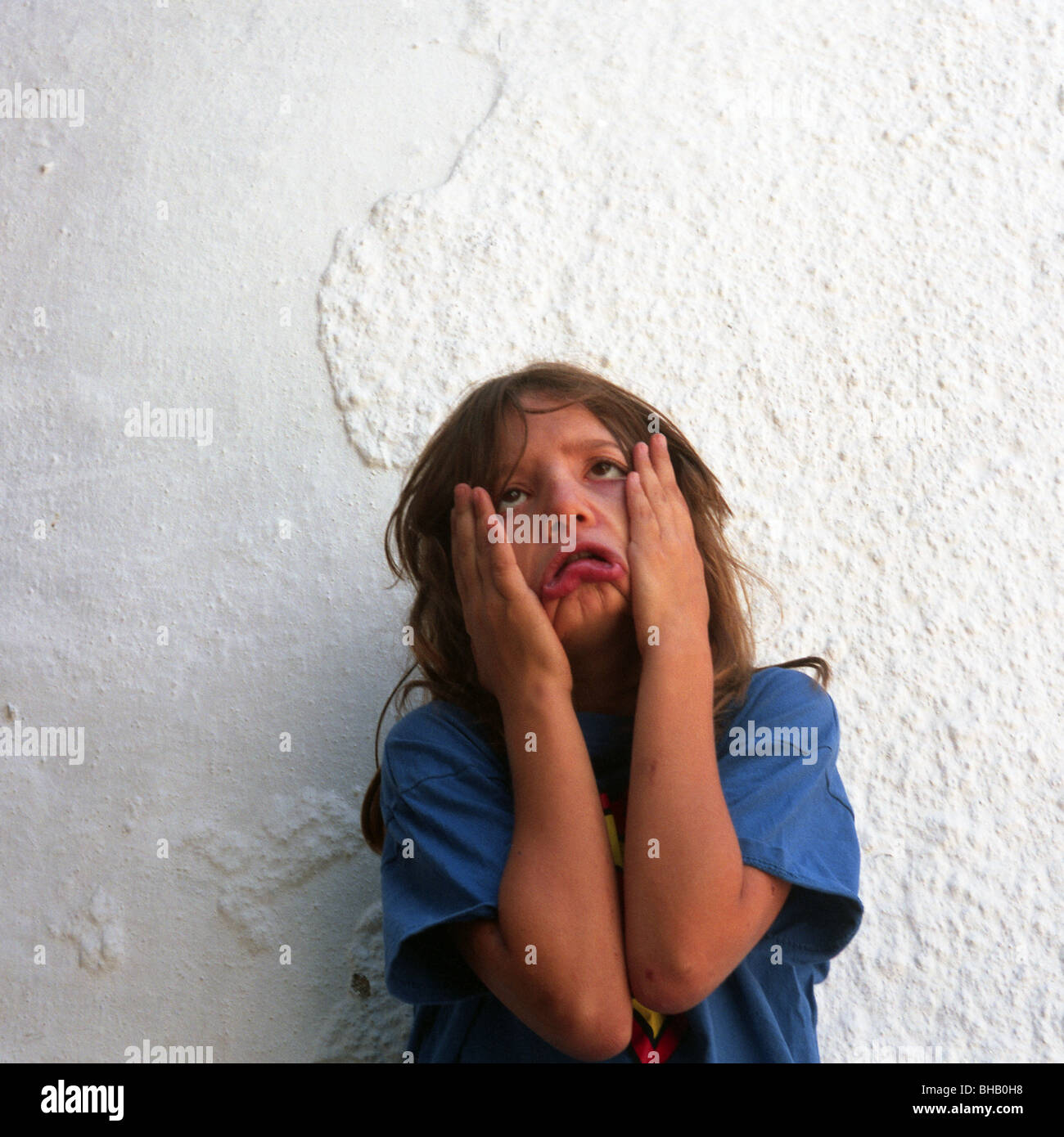 Giovane ragazza di fronte a un muro bianco tirando i volti Foto Stock