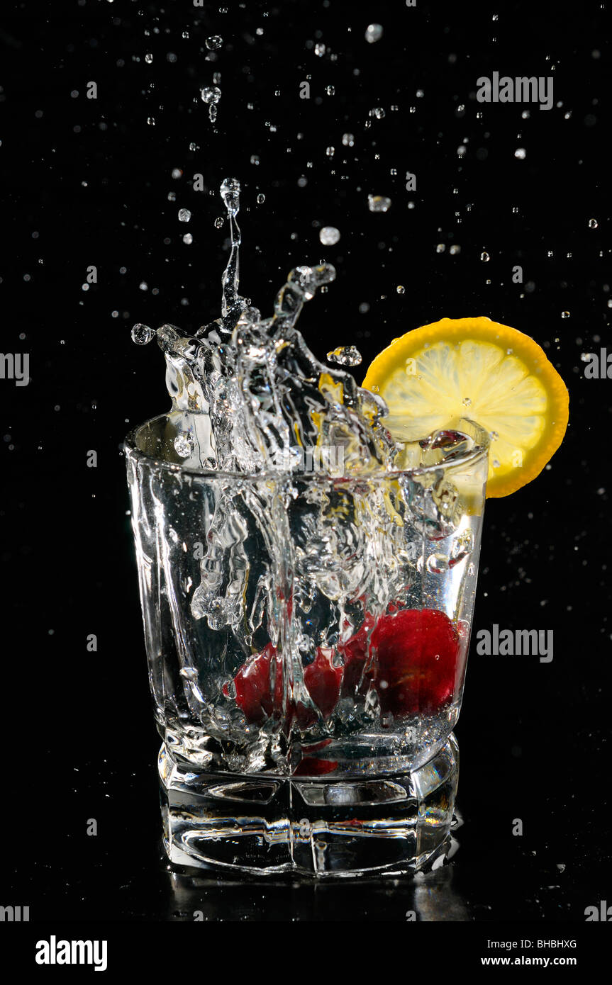 Le ciliegie schizzi in acqua frizzante di vetro con una fetta di limone su sfondo nero Foto Stock