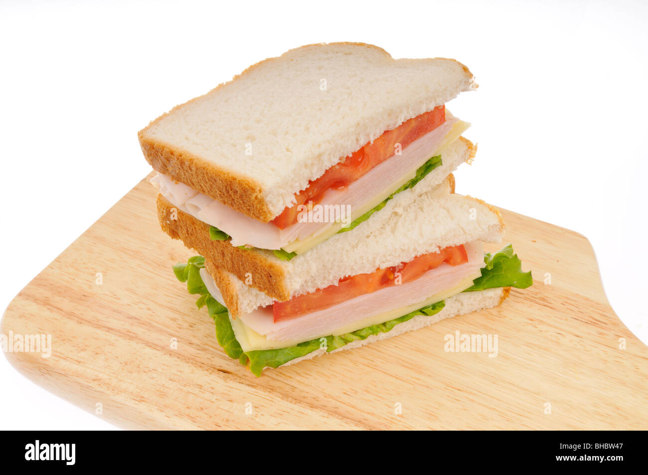 La Turchia e il formaggio sandwiche sul pane bianco con lattuga e tomatoe impilati su un tagliere su sfondo bianco. Foto Stock