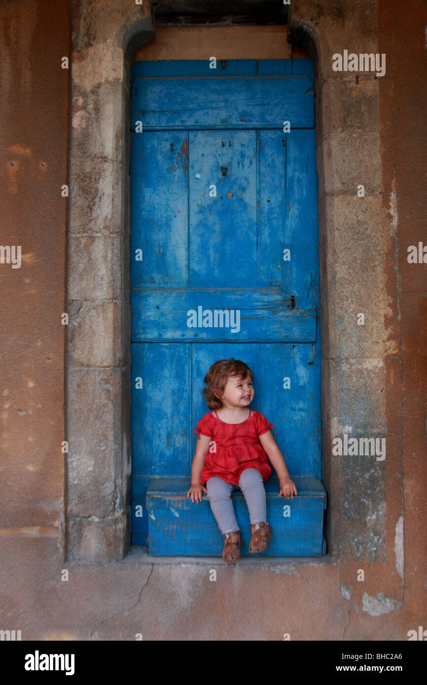 Faustine 19 mese vecchio seduto di fronte a una porta blu in un villaggio della Provenza Foto Stock