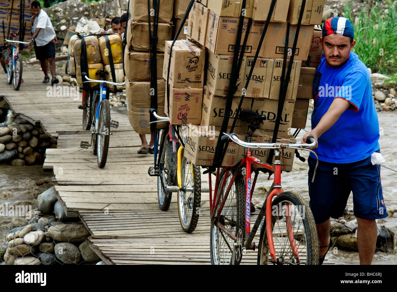 Trafficanti colombiani spingendo le biciclette completamente caricato con il venezuelano sul contrabbando illegale di un ponte che attraversa il fiume di confine. Foto Stock