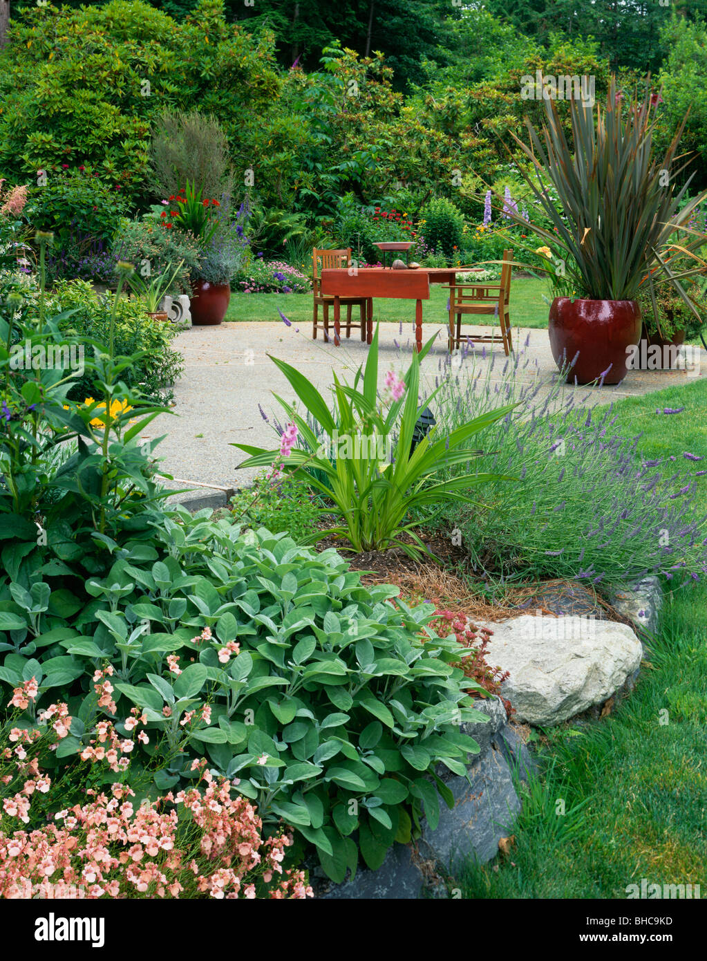 Vashon Island, WA: un patio con tavolo e sedie da giardino circondato da giardini fioriti e grande e colorata di piante in vaso Foto Stock