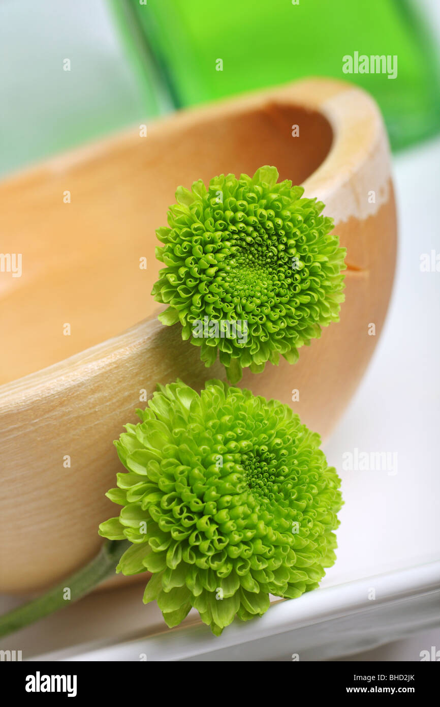 Ciotola di legno decorate con fiori di crisantemo, verde con oli da bagno in background. Foto Stock