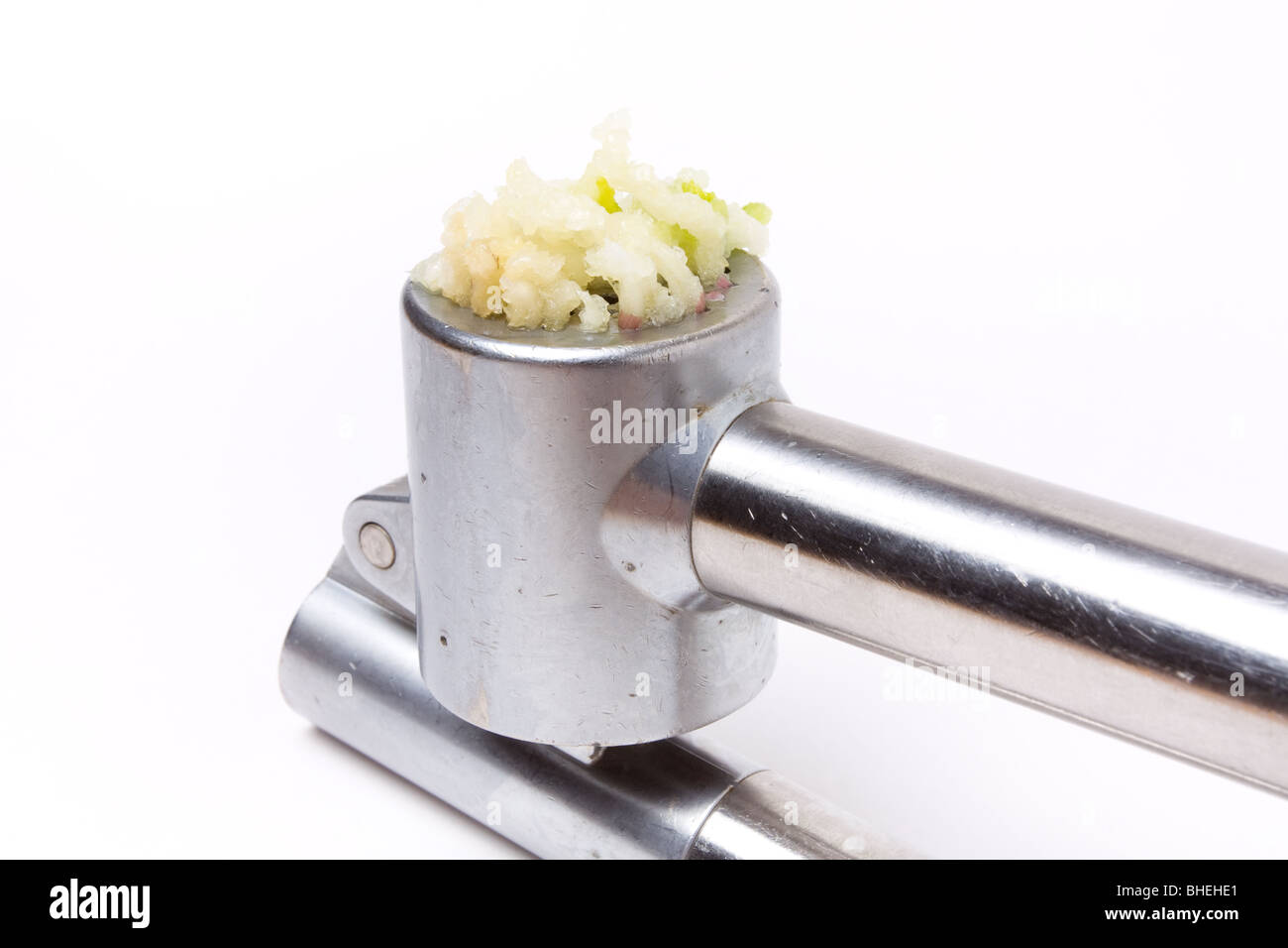 Aglio schiacciato colava da un argento lucido aglio premere isolata contro uno sfondo bianco. Foto Stock