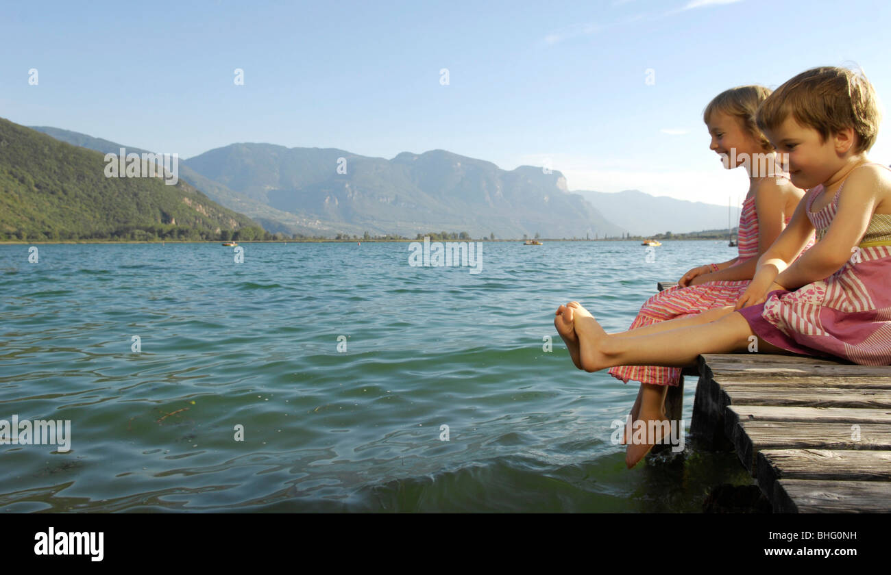 Due ragazze seduto su di un molo a un lago sotto la luce diretta del sole, Lago di Caldaro, Alto Adige, Italia, Europa Foto Stock