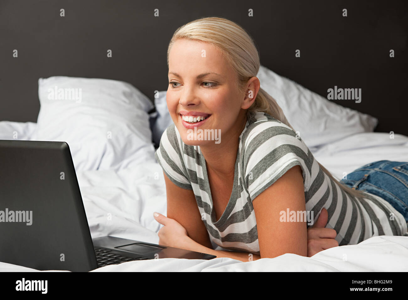 Giovane donna sdraiata sul letto con il computer portatile Foto Stock