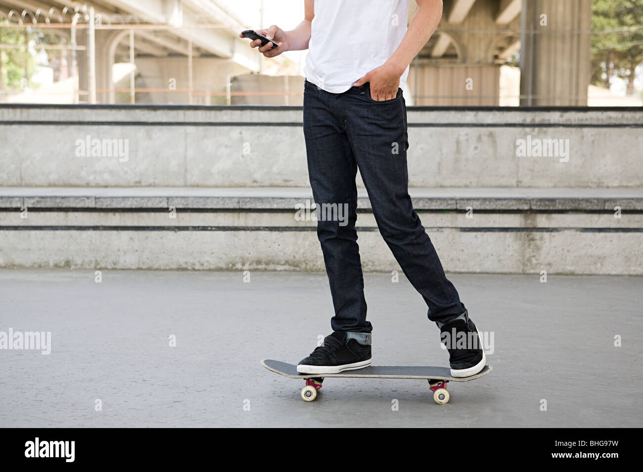 Ragazzo adolescente su skateboard con il cellulare Foto Stock
