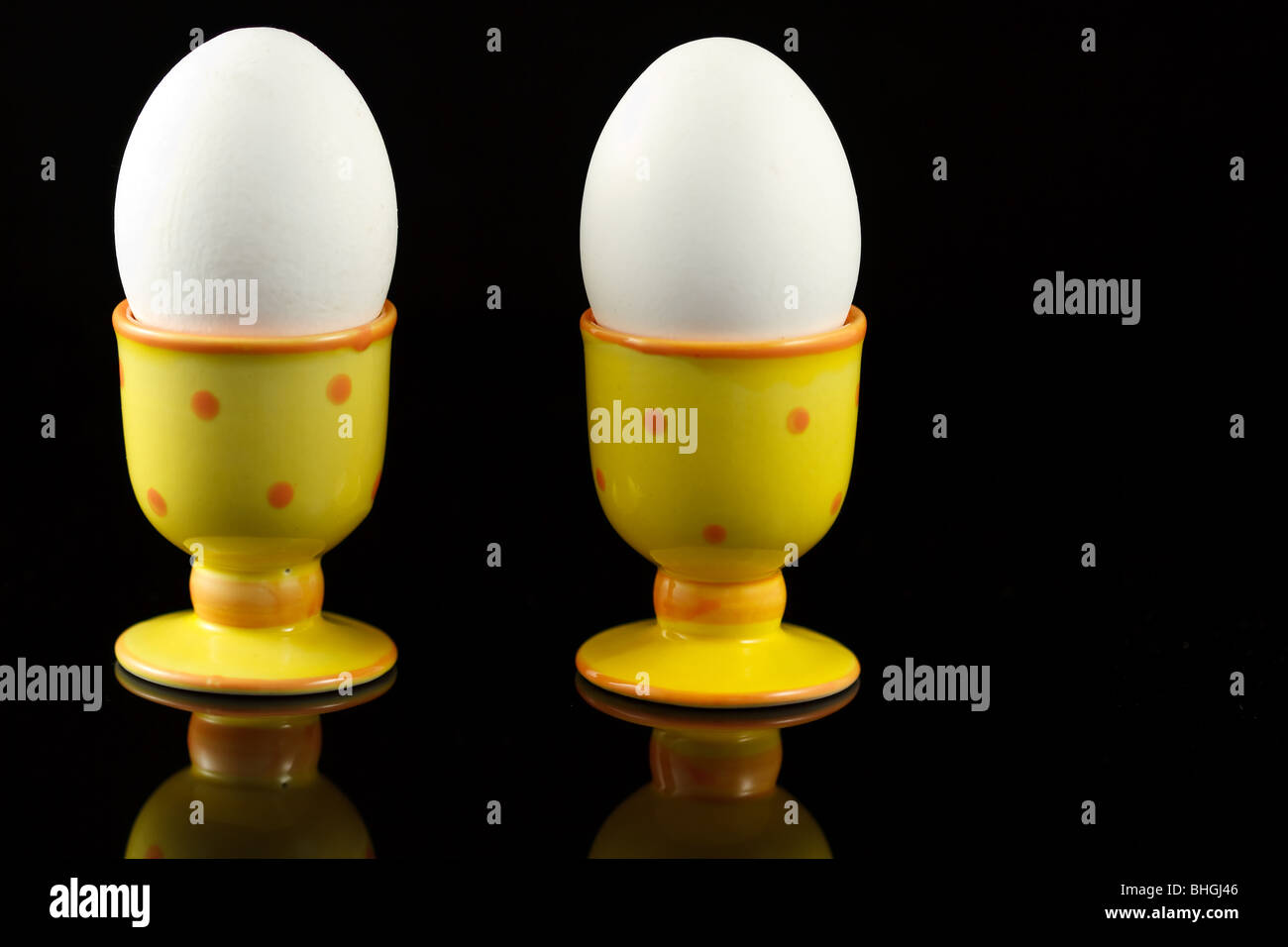 Le uova di gallina in eggcups punteggiata riflettendo su sfondo nero Foto Stock