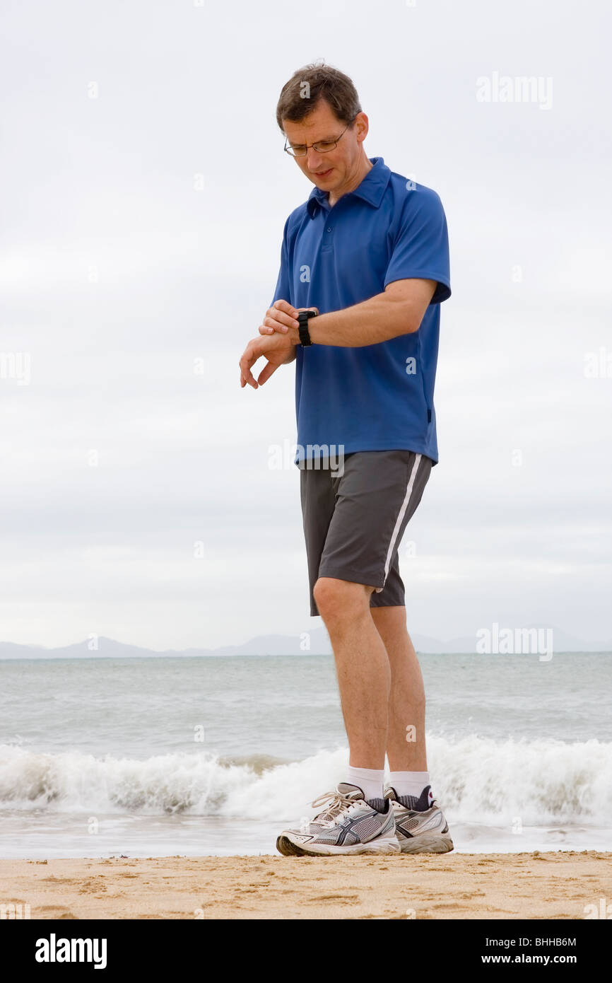 Runner guardando il cronometro su una spiaggia Foto Stock