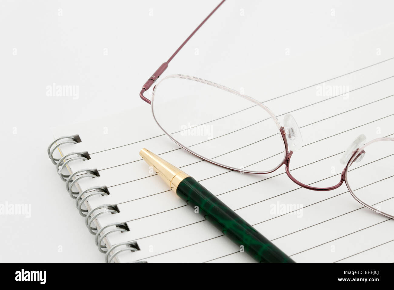 Close-up di un vuoto di carta rivestito con rilegatura a spirale il blocco note per notebook con una penna a sfera e un paio di occhiali su un semplice sfondo bianco per copyspace Foto Stock