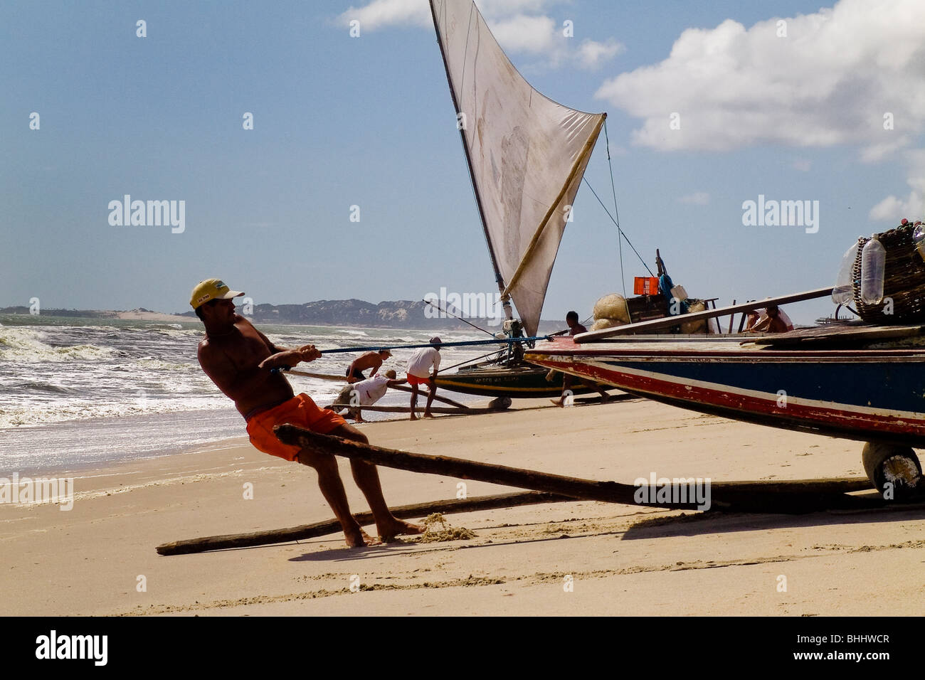 Un pescatore brasiliano di spingere la barca con tronchi di legno verso l'oceano sulla Spiaggia di Prainha, Brasile. Foto Stock