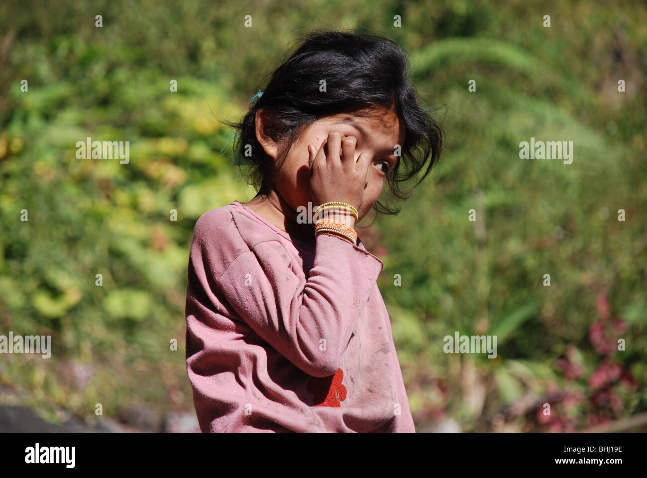 Un bambino nelle zone rurali del Nepal si copre la faccia con la mano Foto Stock