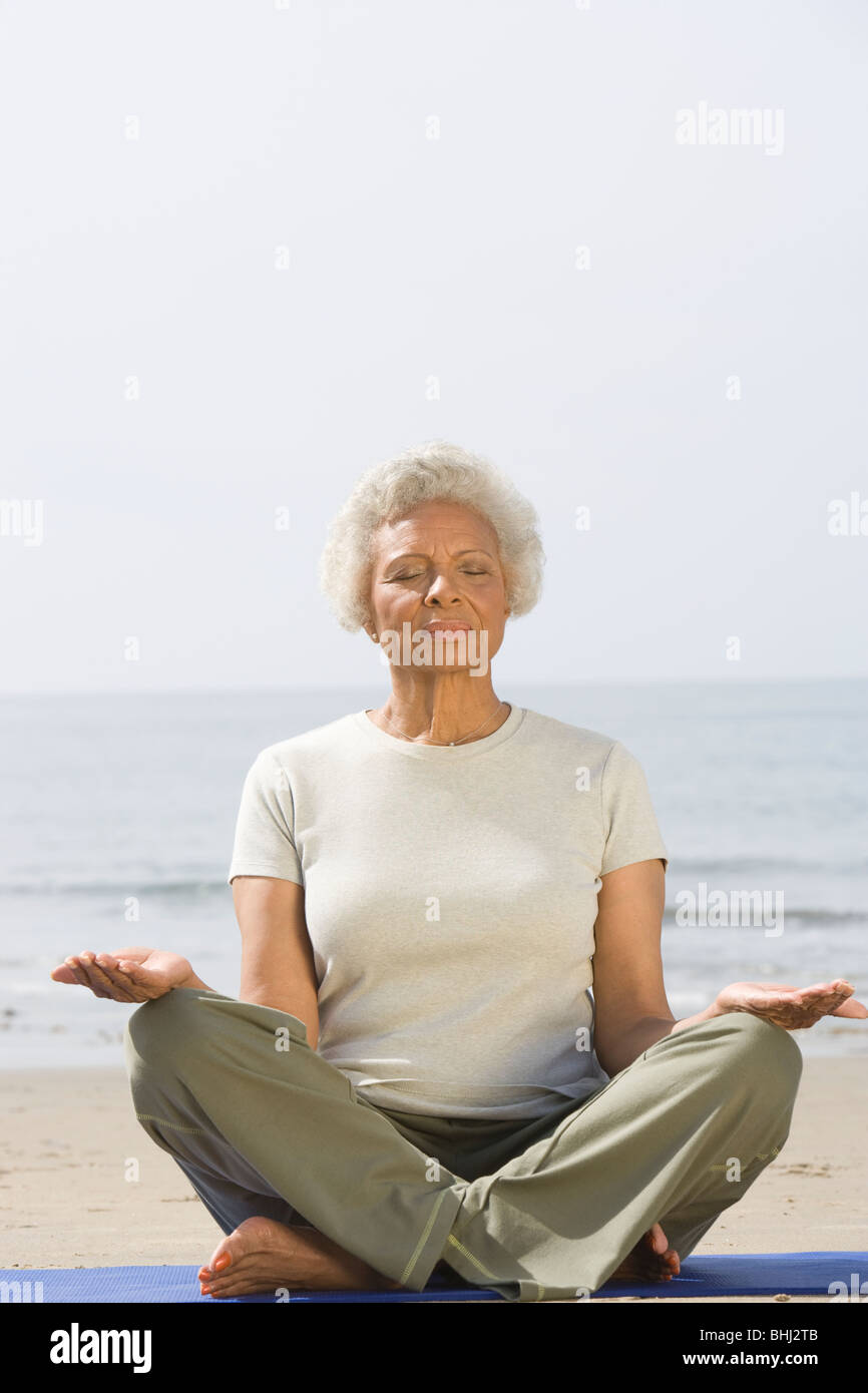 Senior donna si siede con le gambe incrociate nella posa di yoga Foto Stock
