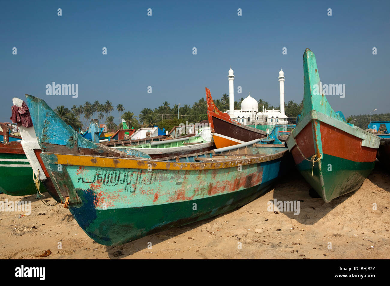 India Kerala, Kovalam, Vizhinjam villaggio pescatori lo scarico di barche di pescatori sulla spiaggia di fronte della nuova moschea bianca Foto Stock
