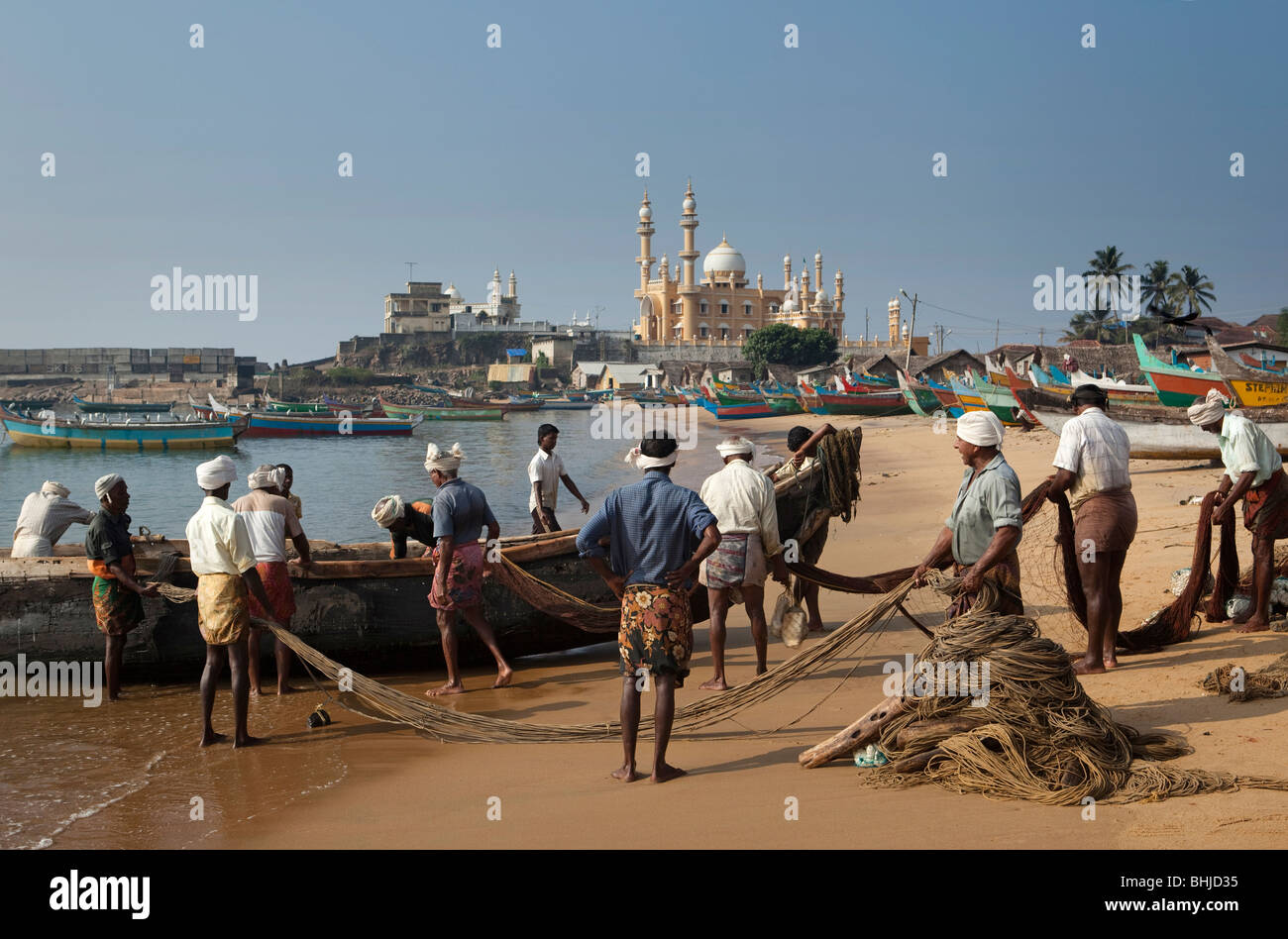 India Kerala, Kovalam, Vizhinjam villaggio pescatori lo scarico di barche di pescatori sulla spiaggia di fronte della moschea Foto Stock