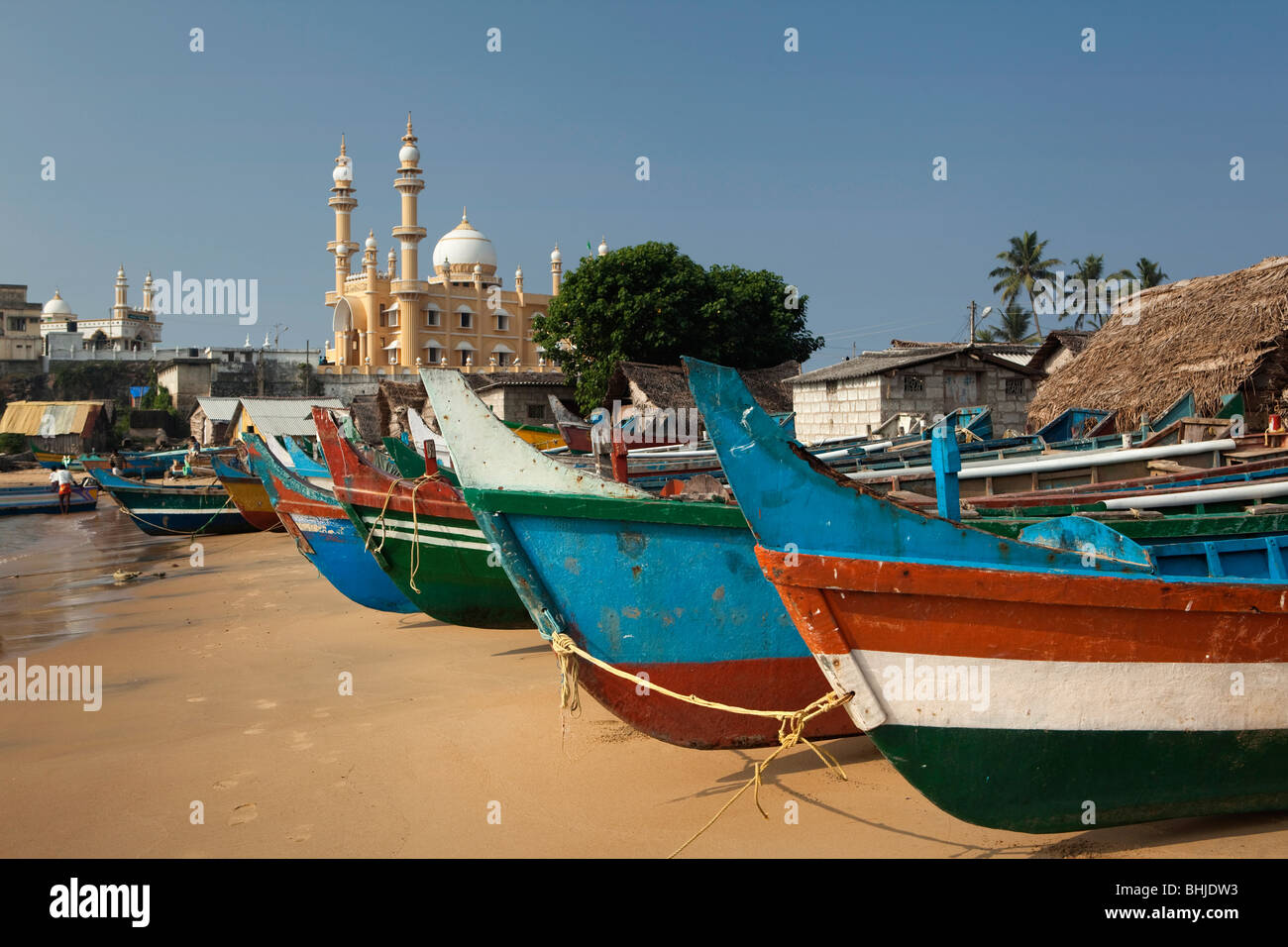 India Kerala, Kovalam, villaggio Vizhinjam coloratissime barche di pescatori sulla spiaggia di fronte della moschea Foto Stock