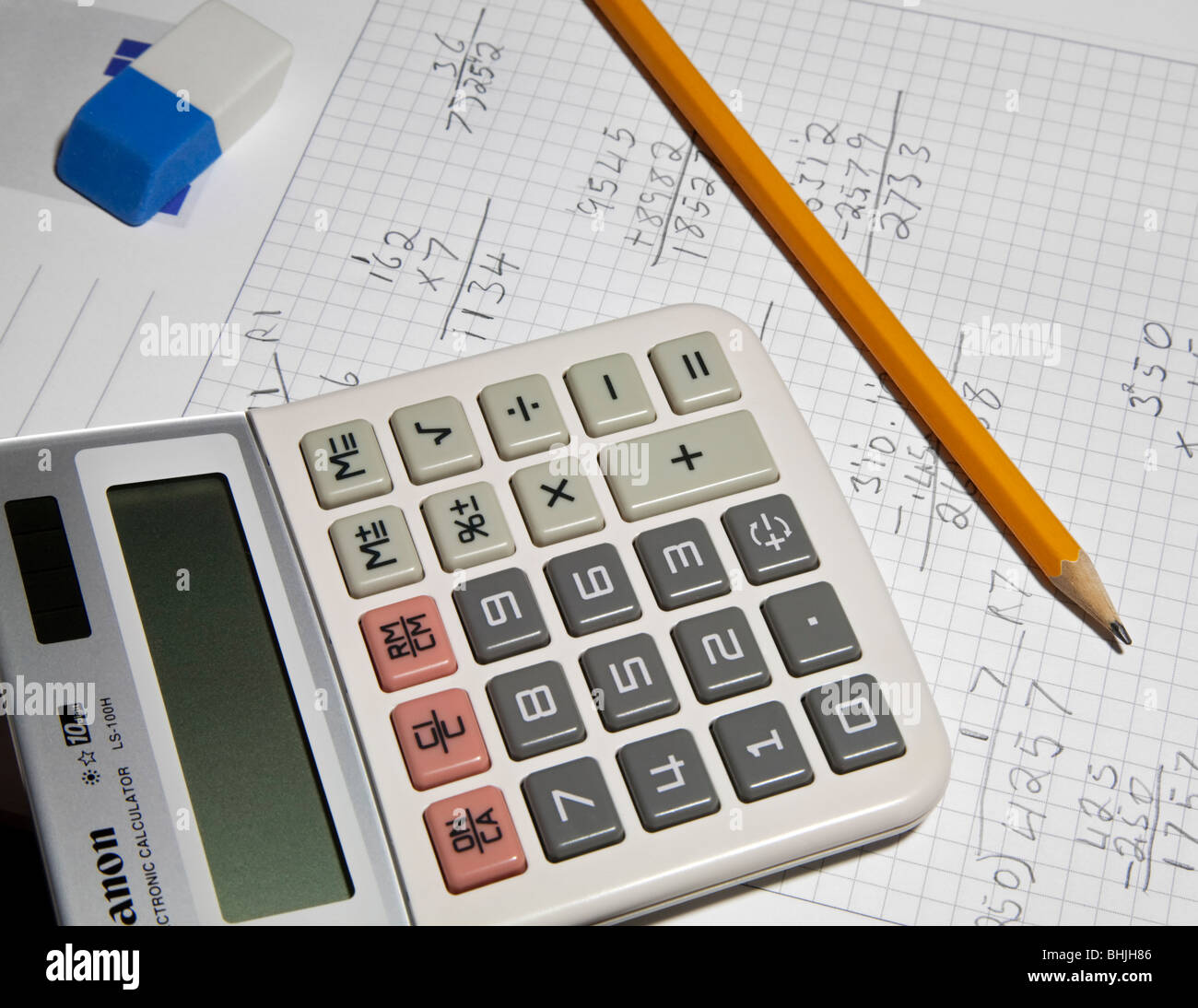 Working out arithmetic sums on a piece of paper with a pencil and calculator. Foto Stock