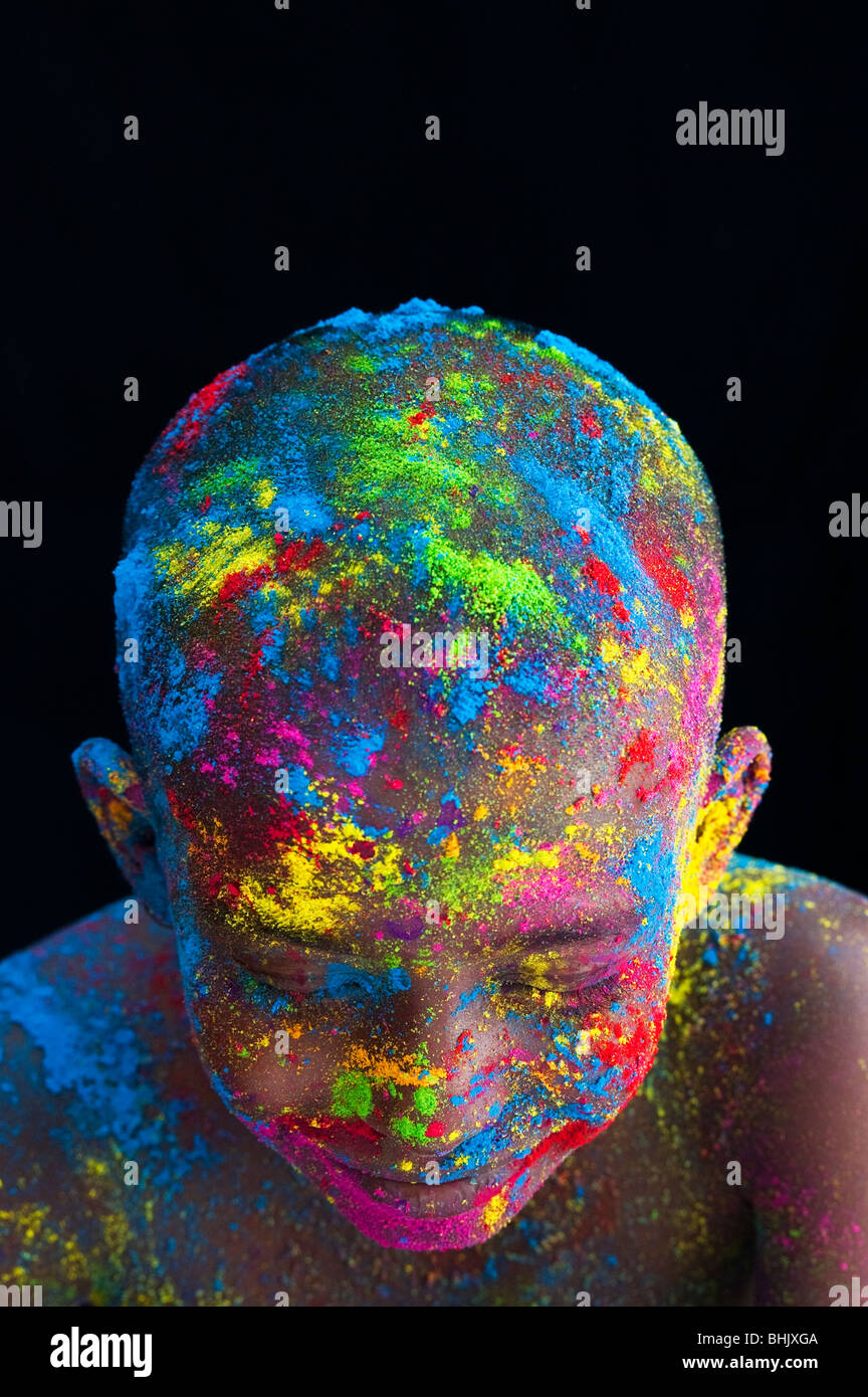 Felice giovane ragazzo indiano coperto di polvere colorata pigmento contro uno sfondo nero Foto Stock