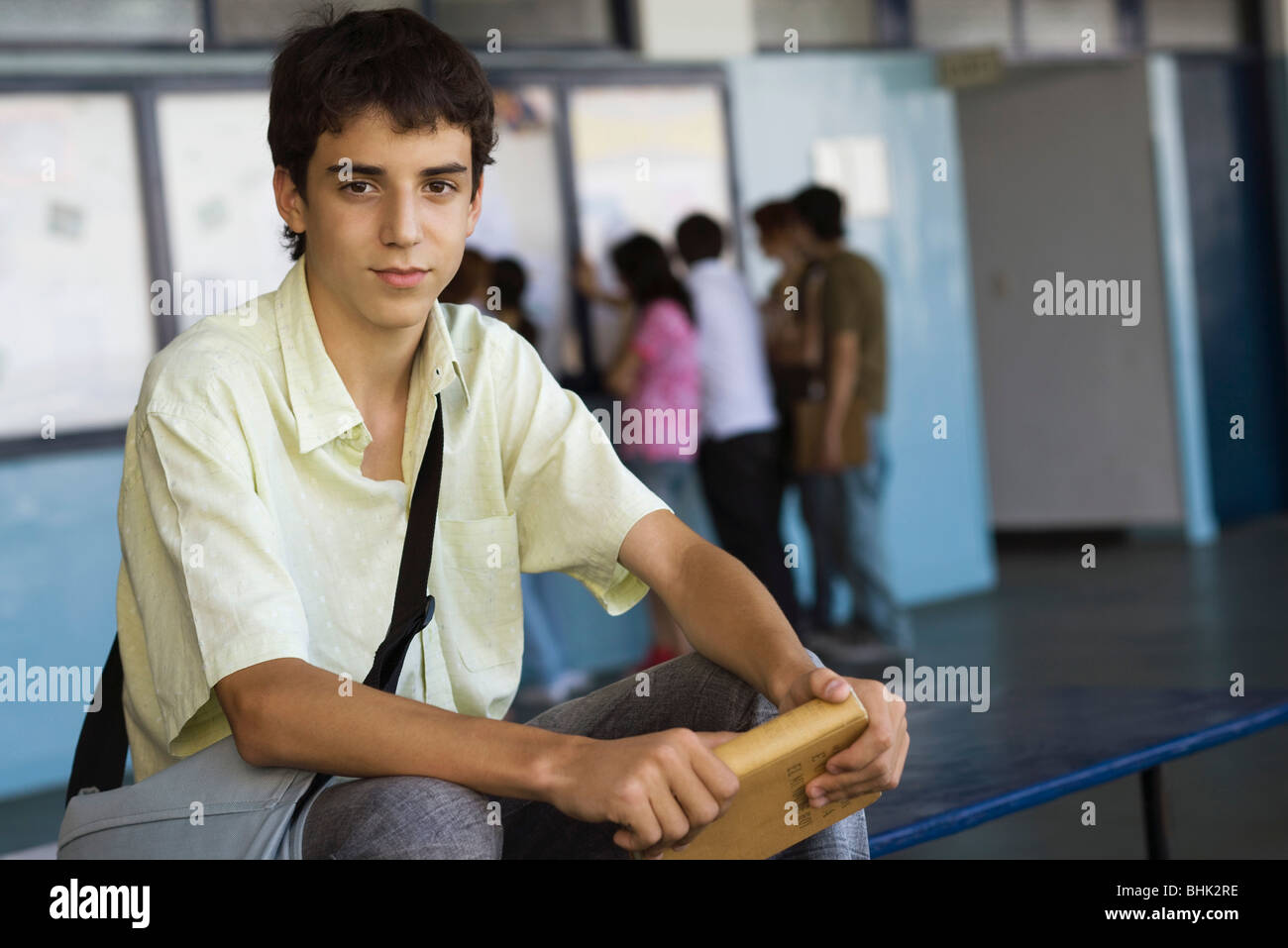 Maschio di alta scuola studente seduto su un banco di lavoro tenendo hardback prenota Foto Stock