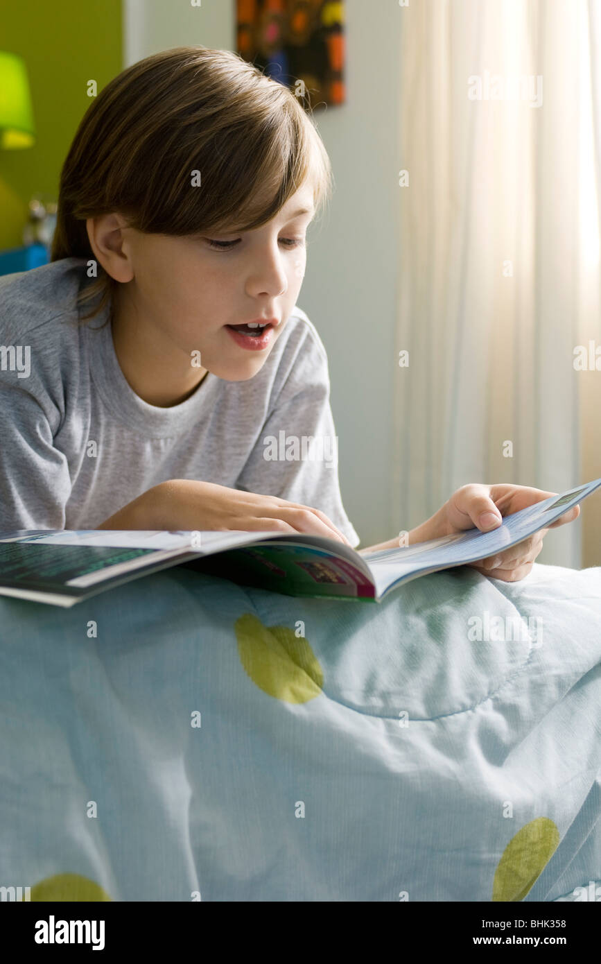 Ragazzo disteso sul letto libro di lettura Foto Stock