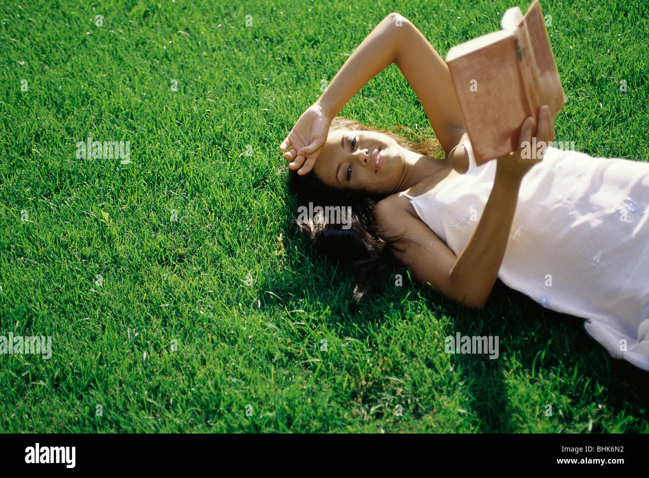 Giovane donna sdraiata su erba, azienda prenota, sorridente in telecamera Foto Stock