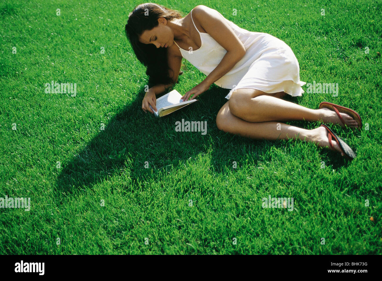 Giovane donna sdraiata su erba libro di lettura Foto Stock