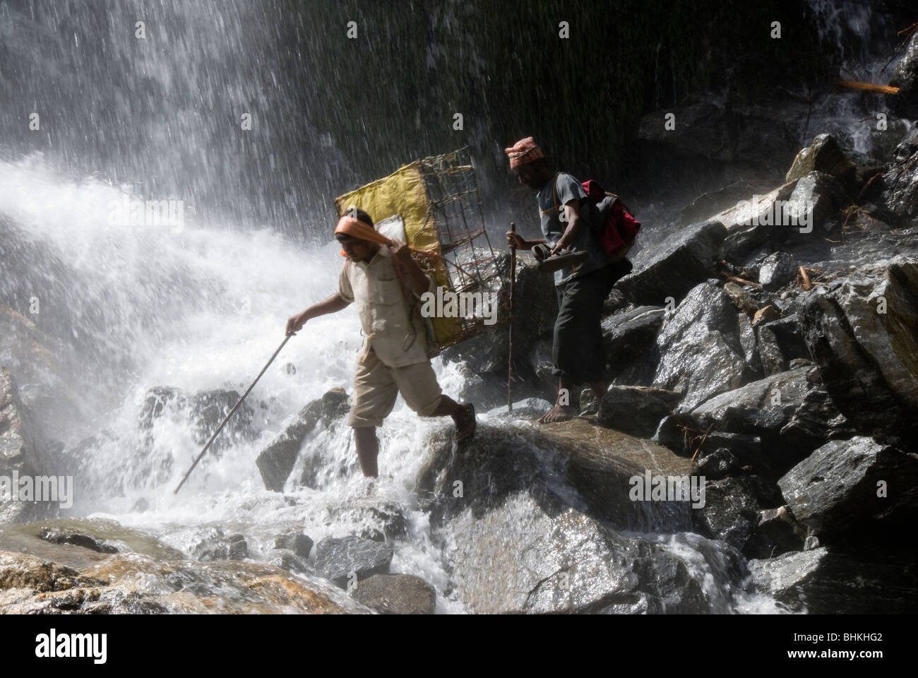 I facchini che trasportano carichi attraverso la cascata, vicino Karte, Circuito di Annapurna, Nepal Foto Stock
