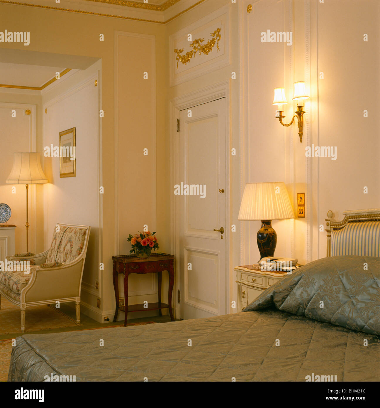 A parete sopra la luce illumina la lampada sul comodino in crema tradizionale townhouse camera da letto con trapunta montato sul basamento Foto Stock