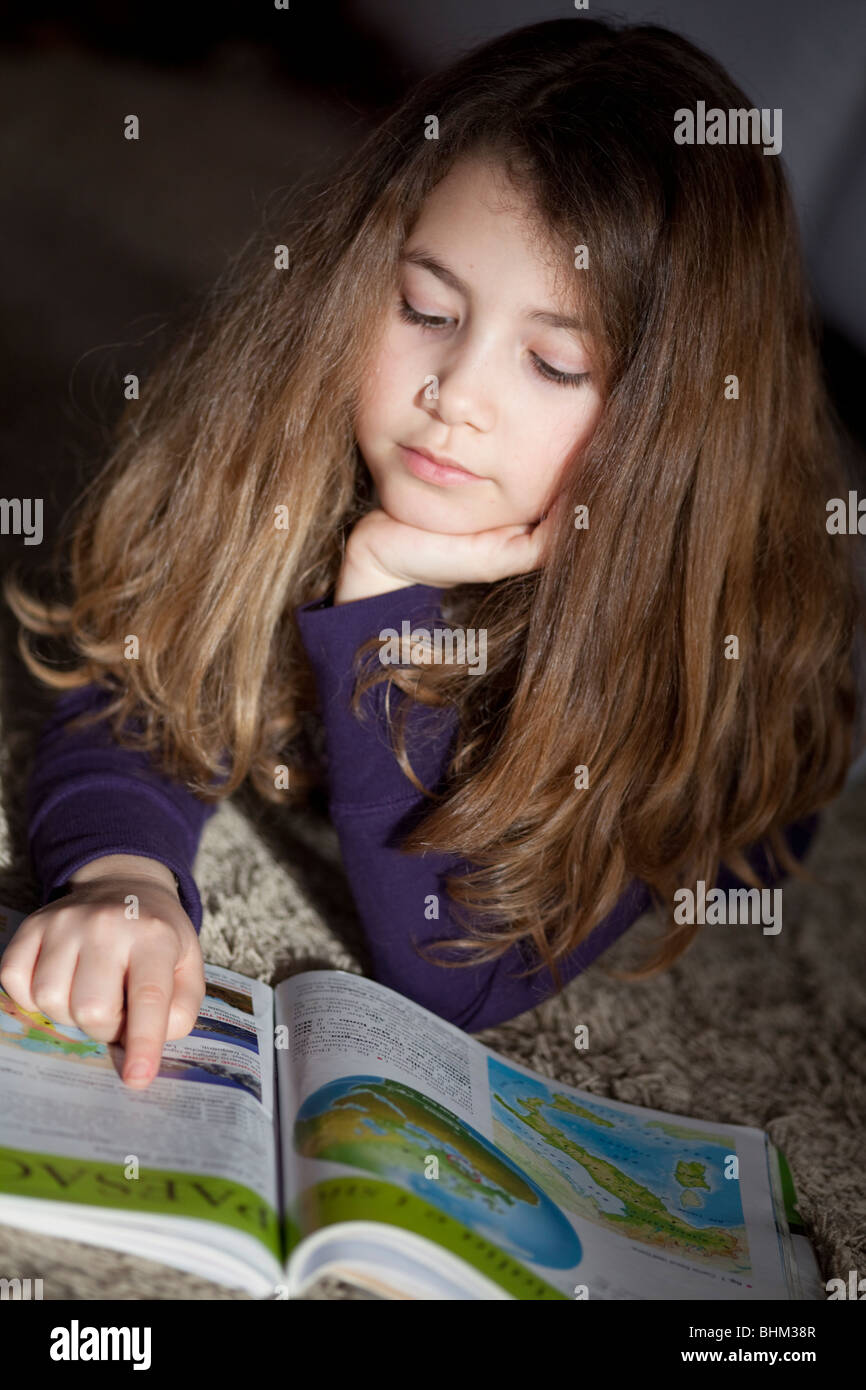 Schoolgirl la lettura di un libro di geografia posa su un tappeto Foto Stock