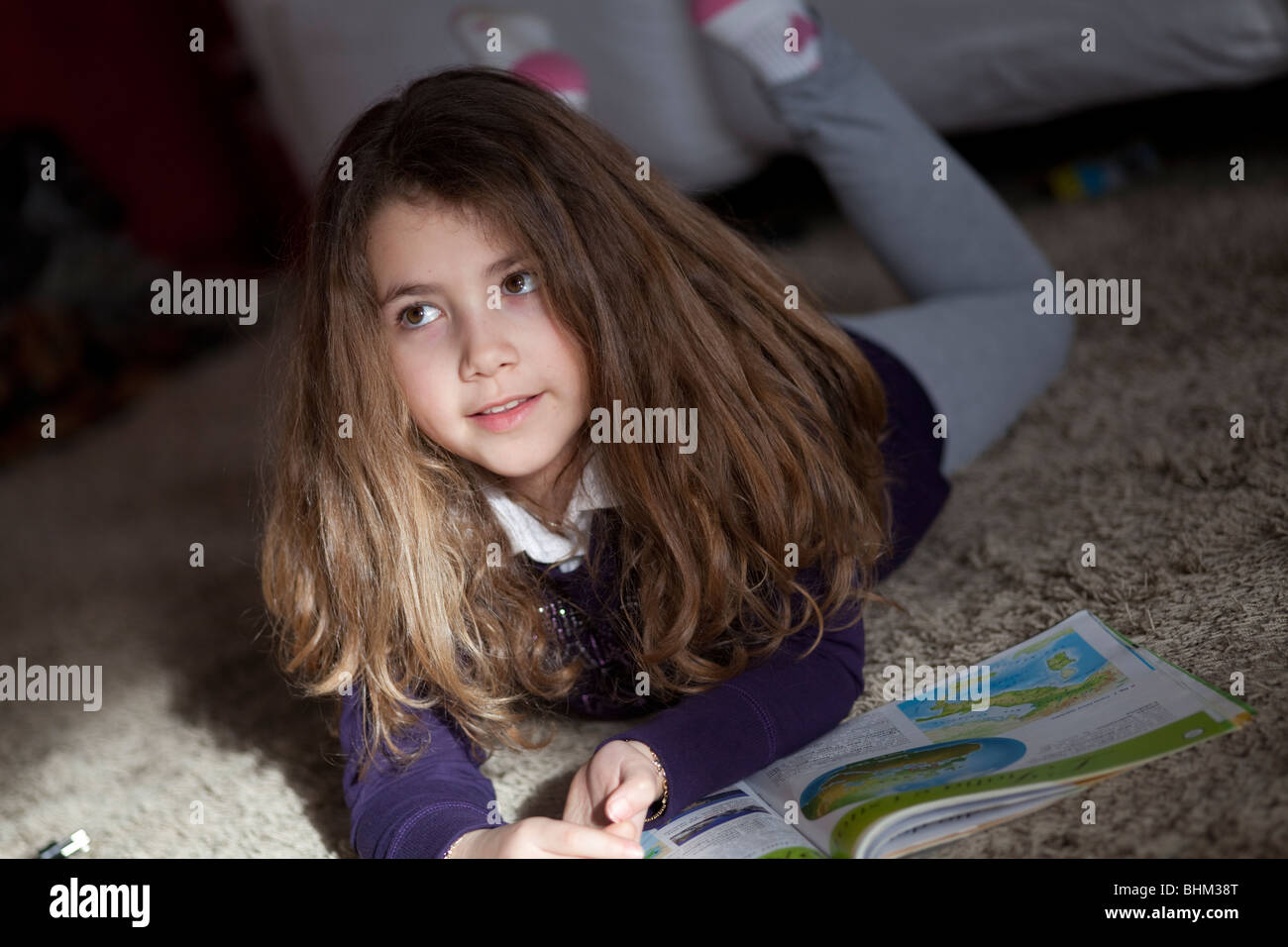 Schoolgirl la lettura di un libro di geografia posa su un tappeto di fronte un divano Foto Stock