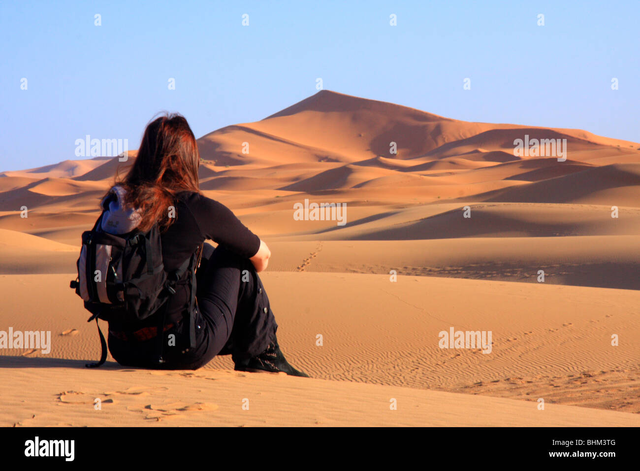 Lone turisti femmina guarda fuori attraverso la Erg Chebbi snad dune nel deserto del Sahara vicino a Merzouga, Marocco Foto Stock