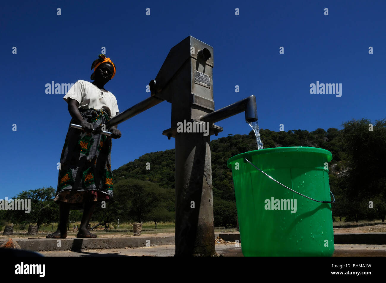 Un abitante di un villaggio utilizzando una pompa a mano rurale per pompare acqua potabile da un pozzo in un villaggio in Malawi Africa Foto Stock