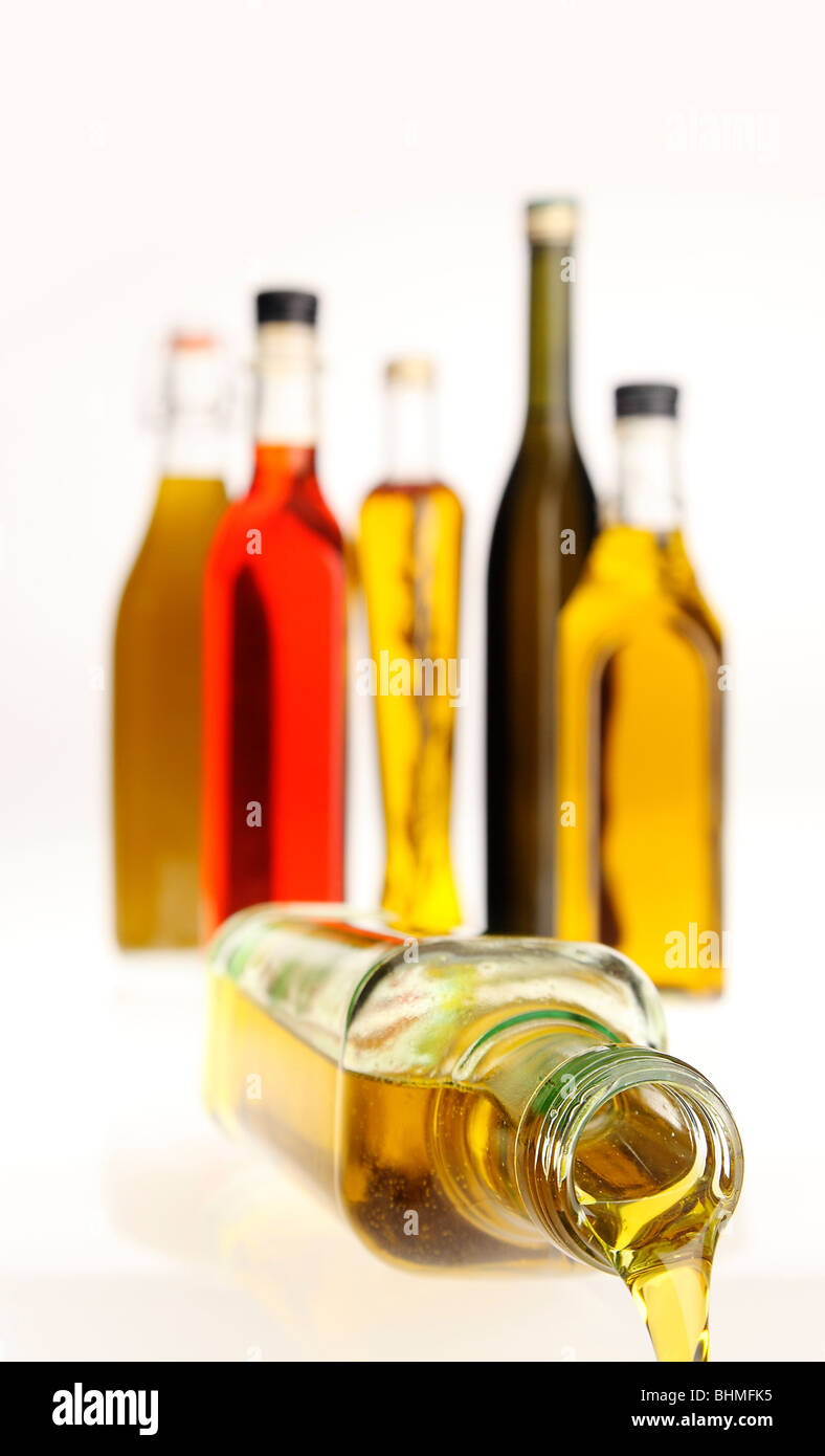 Una bottiglia di olio di oliva di versare, versando al di fuori del telaio con una raccolta di oli minerale dietro, contro uno sfondo bianco. Foto Stock
