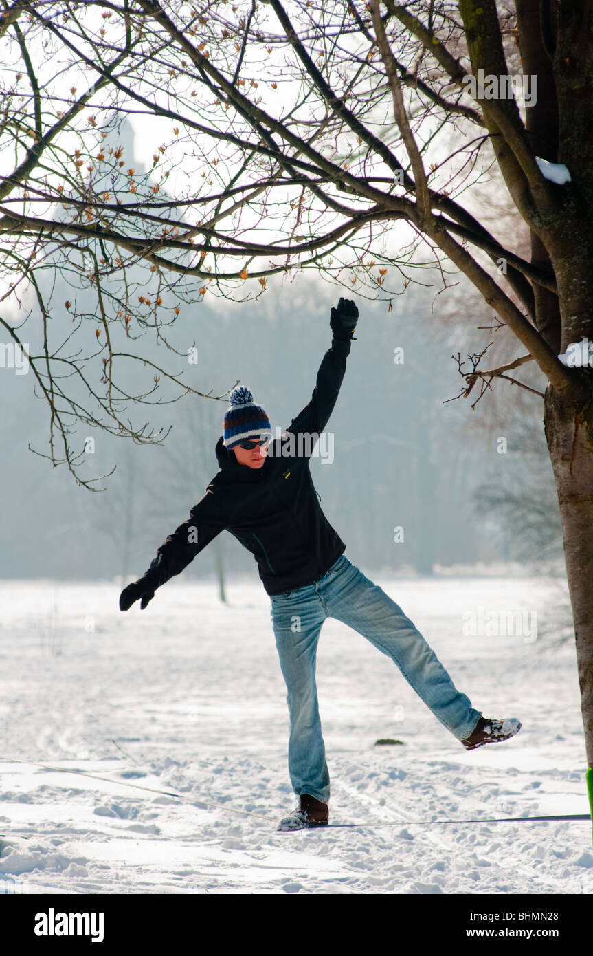 Guy practice equilibrio su una fune in una coperta di neve Giardino Inglese con bavarese della cancelleria dello stato visto in background. Foto Stock