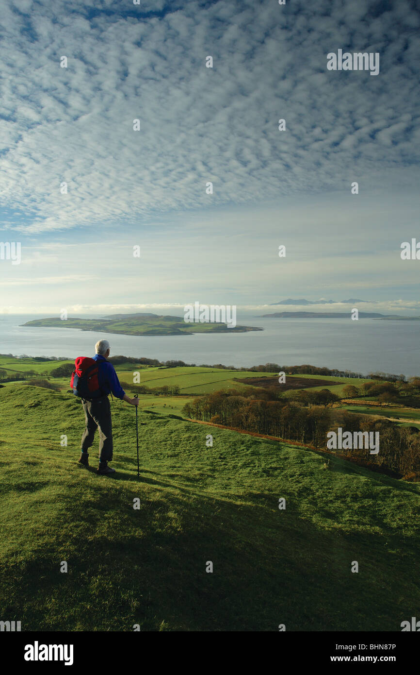 Un viandante guarda verso Arran e Cumbrae dal Knock, un Iron Age Fort sopra Largs sull'Ayrshire sentiero costiero, Scozia Foto Stock