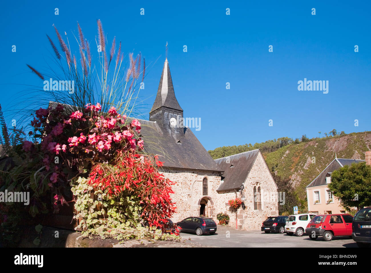 Chiesa e giardino fiorito con le automobili parcheggiate fuori nella Place de l'Eglise, St Leonard des Bois, Pays de la Loire, Francia Foto Stock