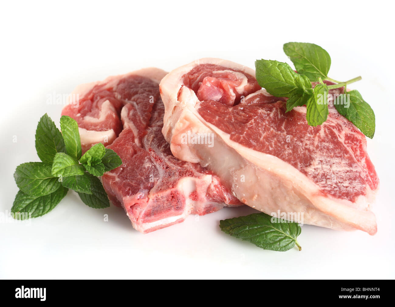 Una coppia di materie costolette di agnello alla menta e uno spicchio di aglio, su una piastra bianca Foto Stock