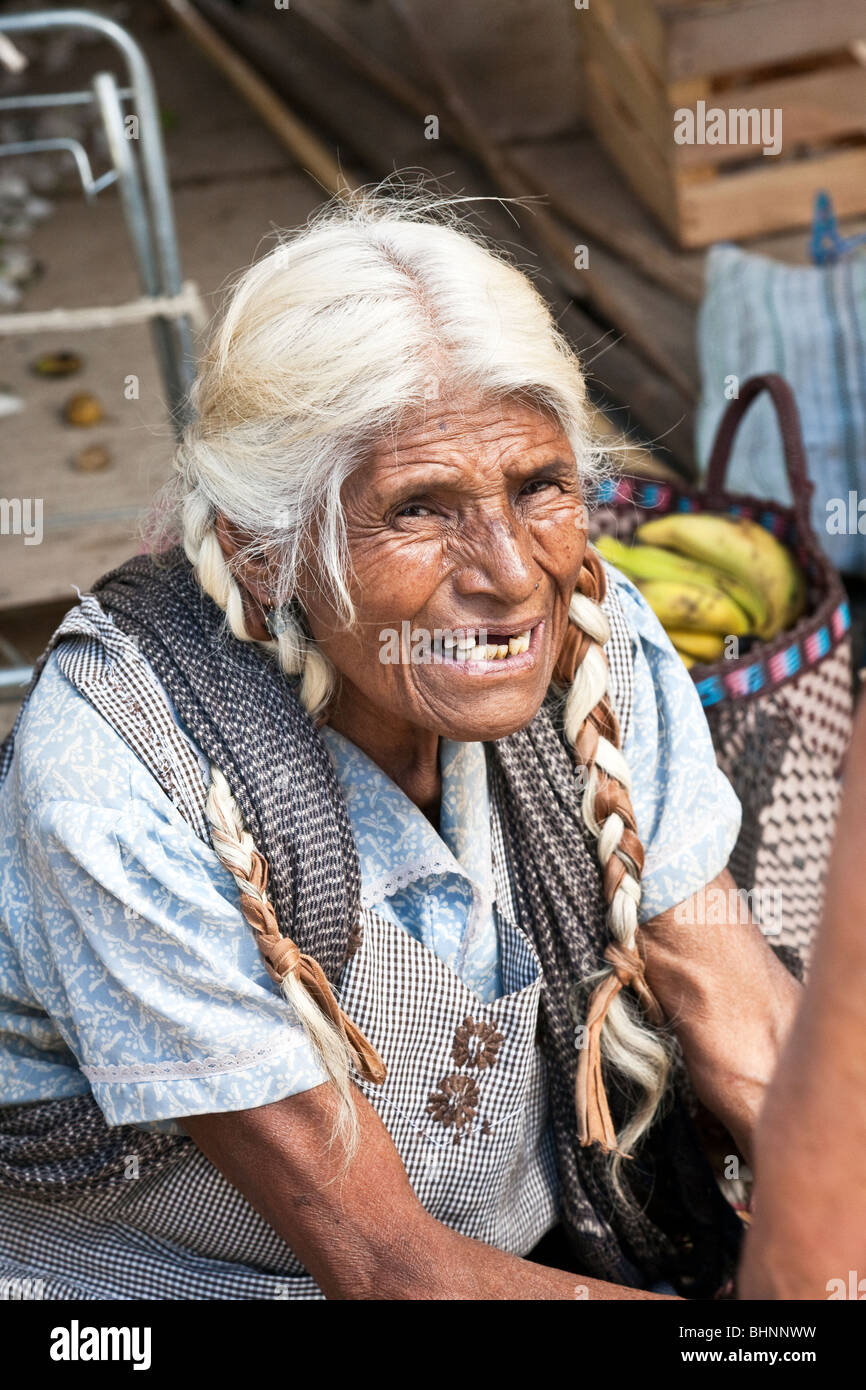 Piuttosto vecchio feroce zapoteco donna con strisce di tessuto intrecciati con i suoi capelli nevosi haggles con un cliente al mercato Ocotlan Oaxaca Foto Stock