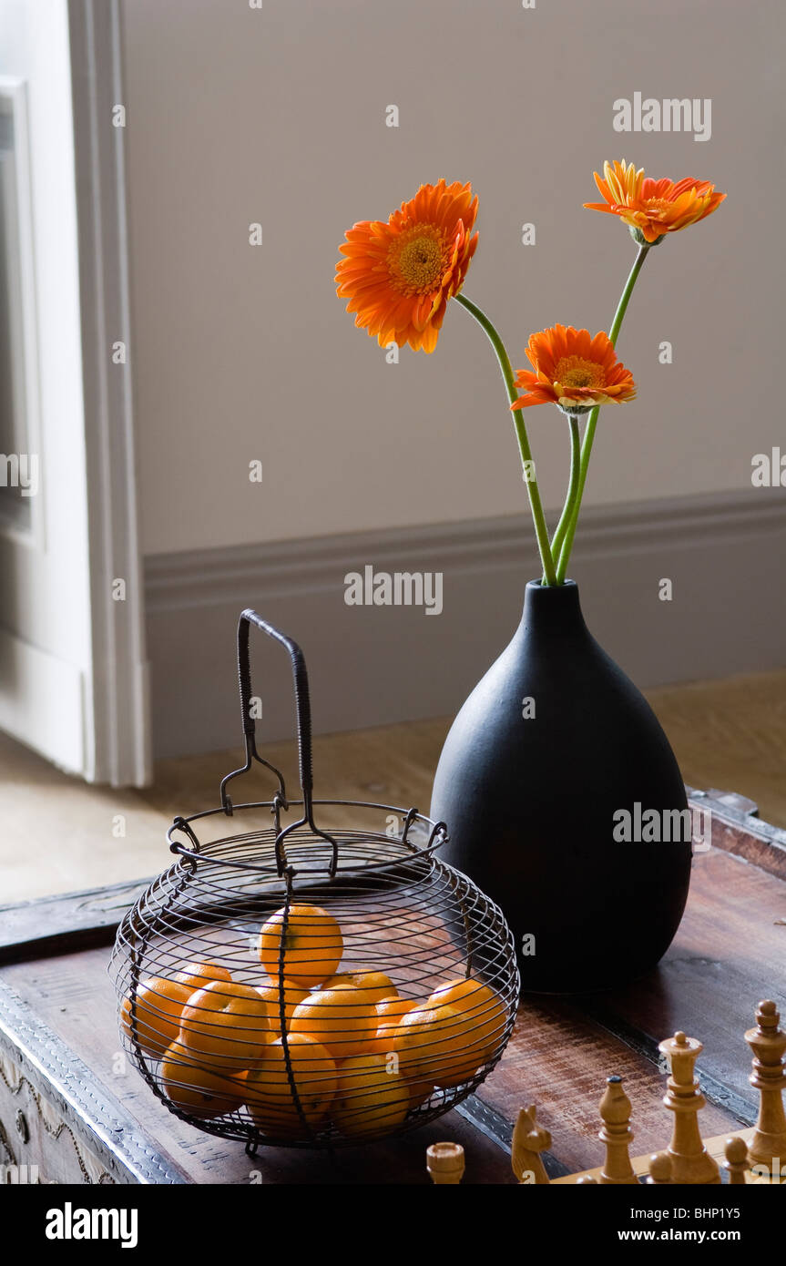 Orange gerbera fiori in vaso nero sul piano portapaziente con il cestello di metallo Foto Stock