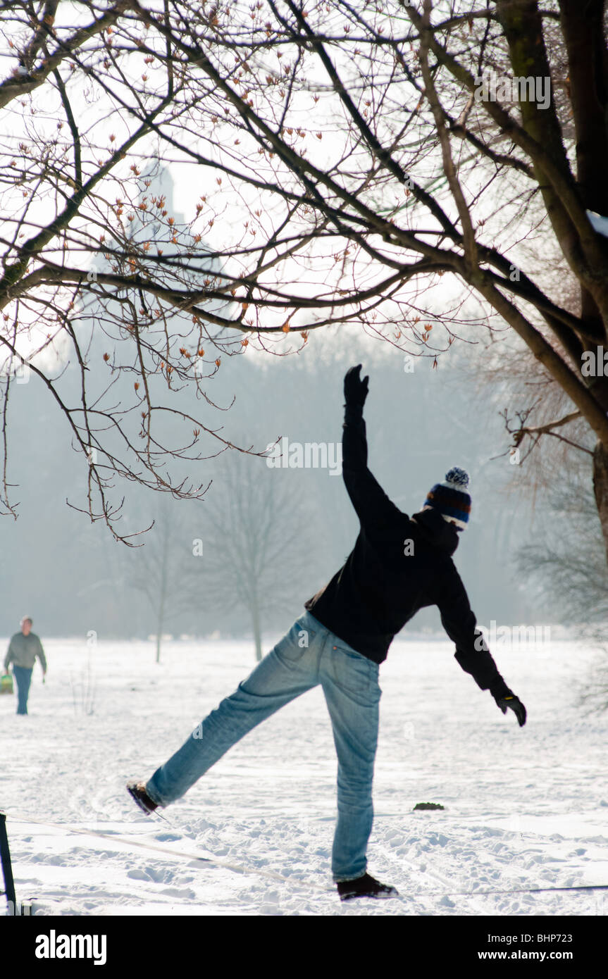 Un ragazzo in equilibrio su una corda in una coperta di neve Giardino Inglese con bavarese della cancelleria dello stato visto in background Foto Stock