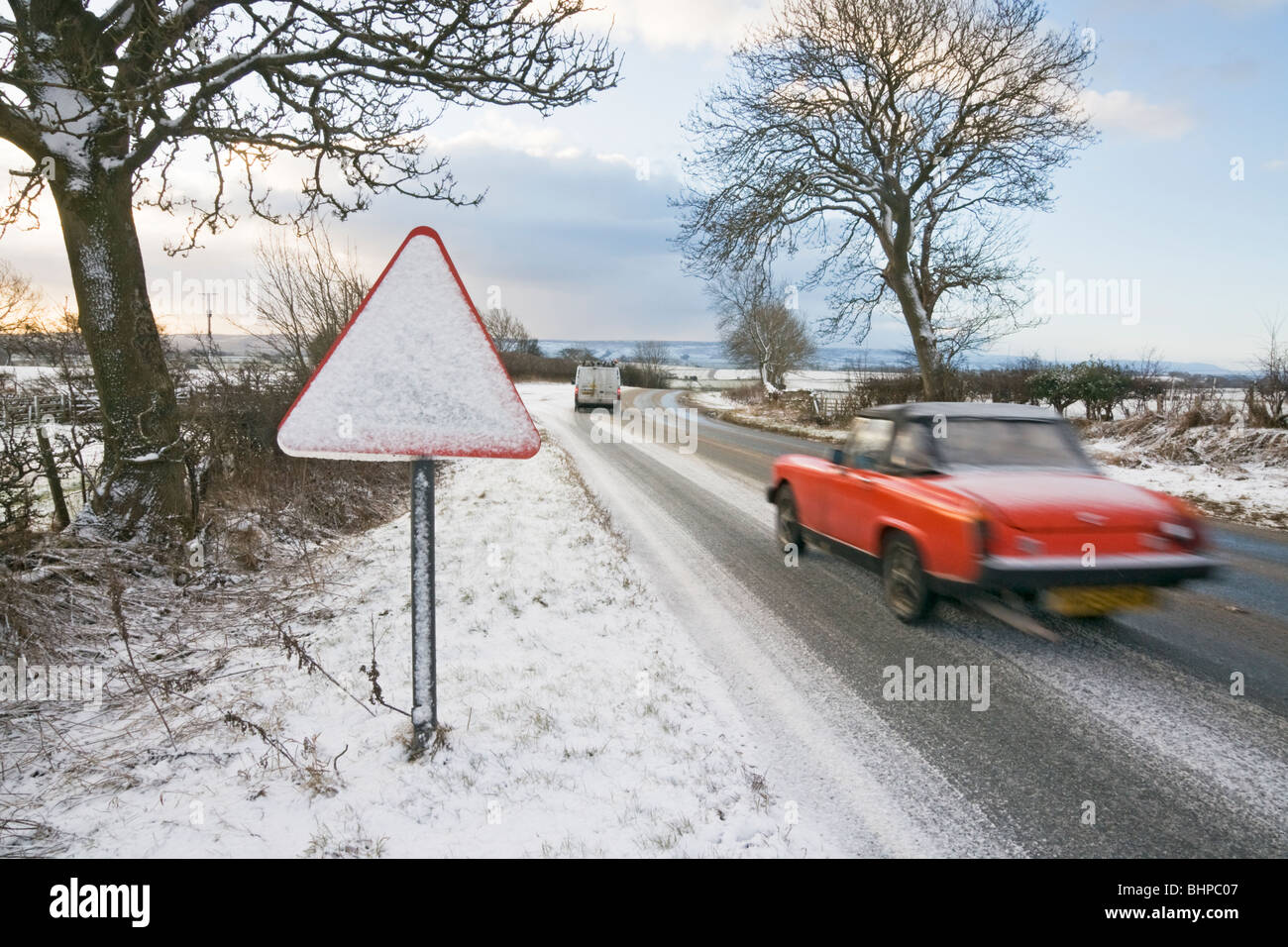 Strada segno di avvertimento coperte di neve a fianco di una granita coperto Road, North Yorkshire, Regno Unito Foto Stock