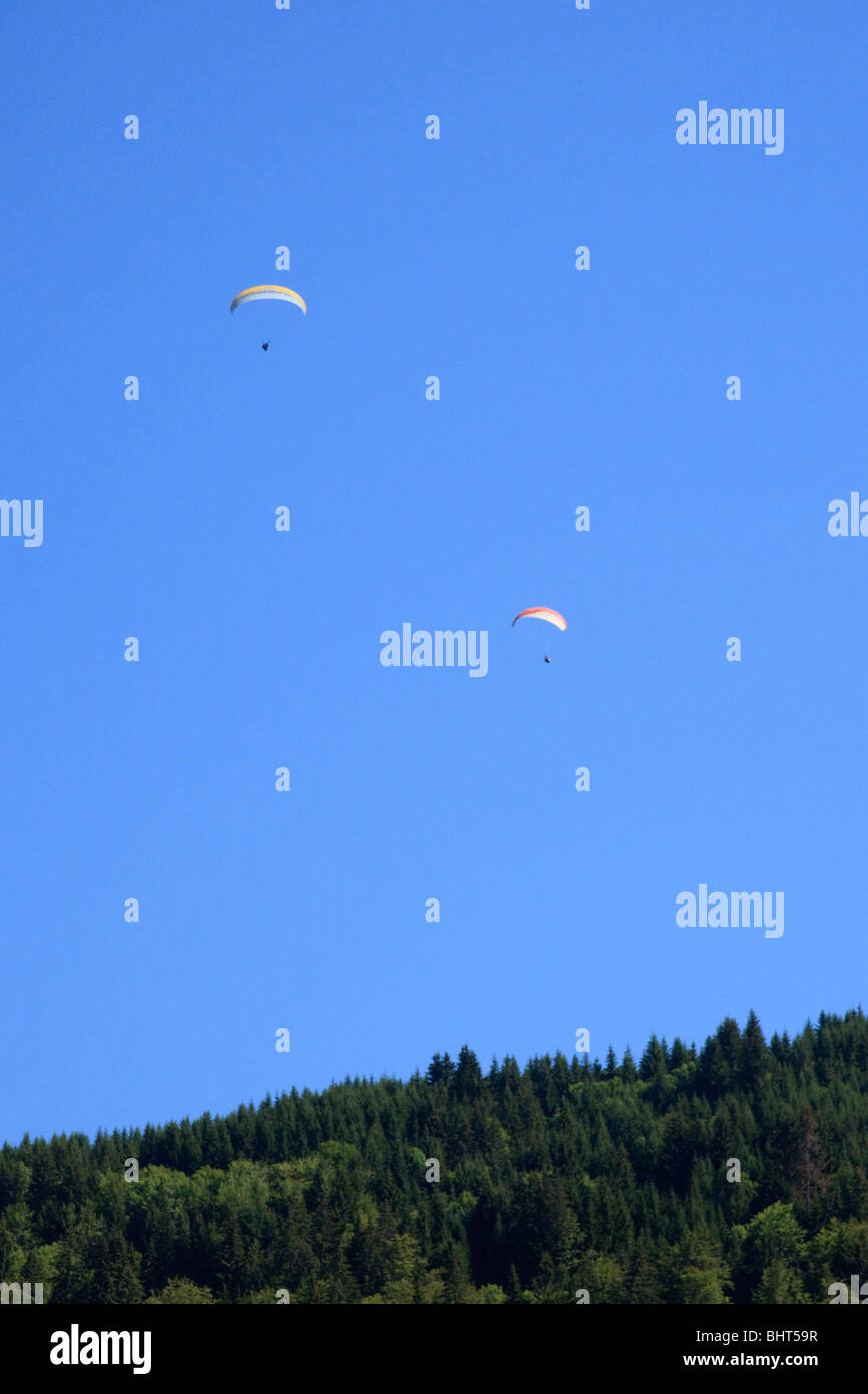Due parapendii contro un cielo blu sopra gli alberi nelle Alpi francesi Foto Stock